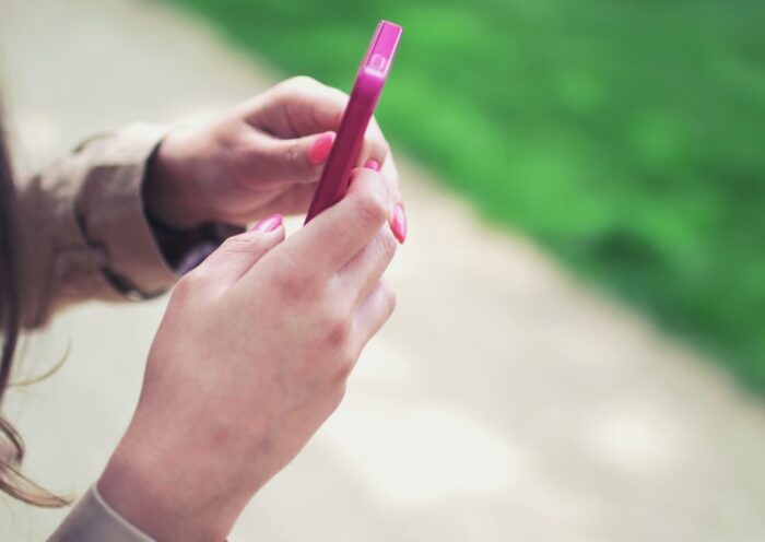 Woman holding a pink smartphone with both hands in a casual outdoor setting