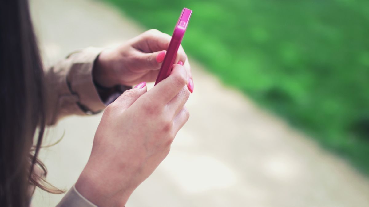 Woman holding a pink smartphone with both hands in a casual outdoor setting