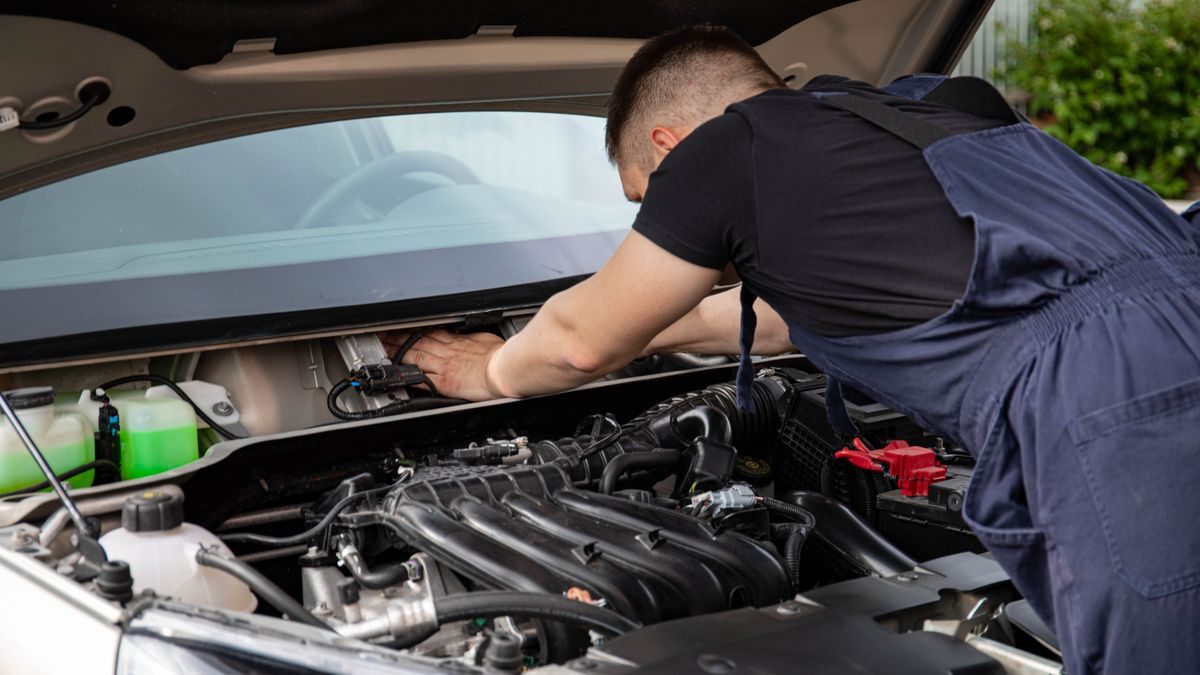 Auto mechanic performs engine maintenance on a car. Focus on hands and engine components