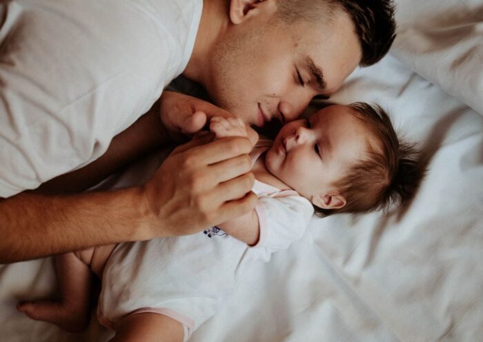 A tender moment of a father bonding with his newborn baby, lying on a bed