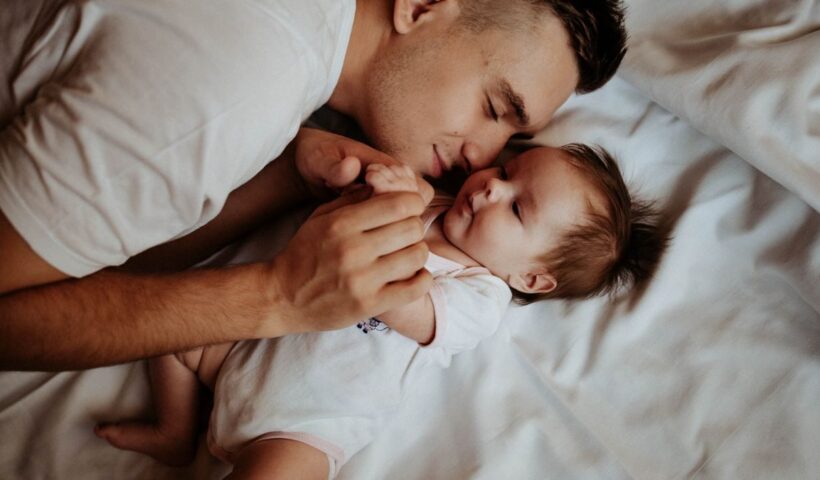 A tender moment of a father bonding with his newborn baby, lying on a bed