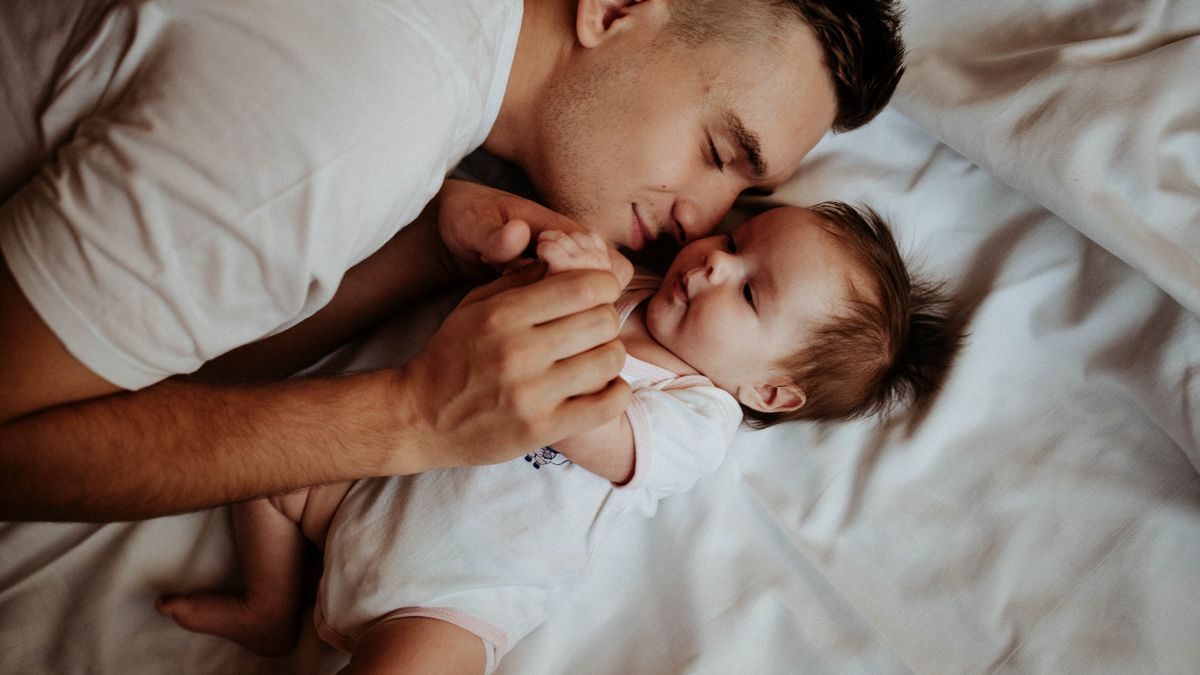 A tender moment of a father bonding with his newborn baby, lying on a bed