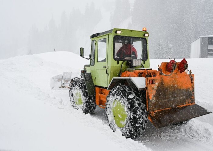 Green and orange snowplow clearing heavy snow in a snowstorm on a frosty day