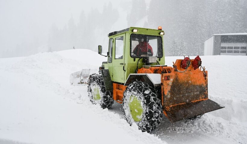Green and orange snowplow clearing heavy snow in a snowstorm on a frosty day