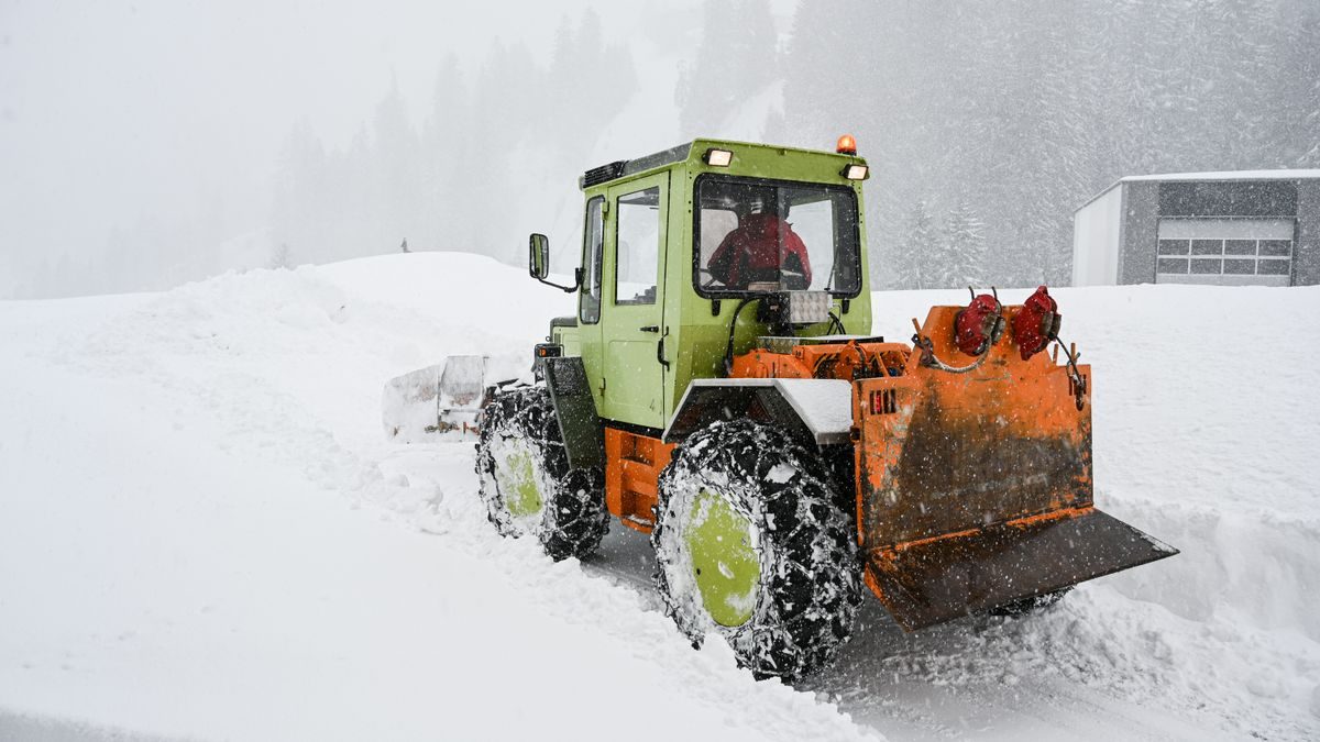 Green and orange snowplow clearing heavy snow in a snowstorm on a frosty day