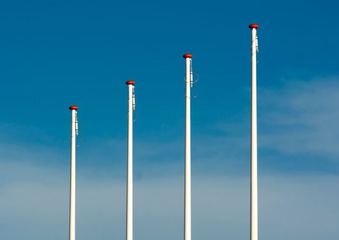 Four tall flag poles stand under a clear blue sky with minimal clouds