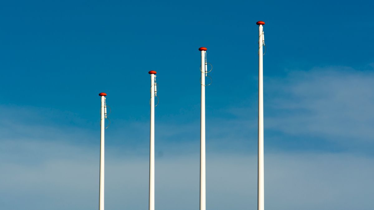 Four tall flag poles stand under a clear blue sky with minimal clouds