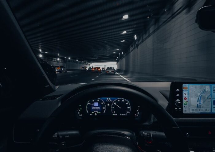 View from car dashboard driving through an illuminated city tunnel at night
