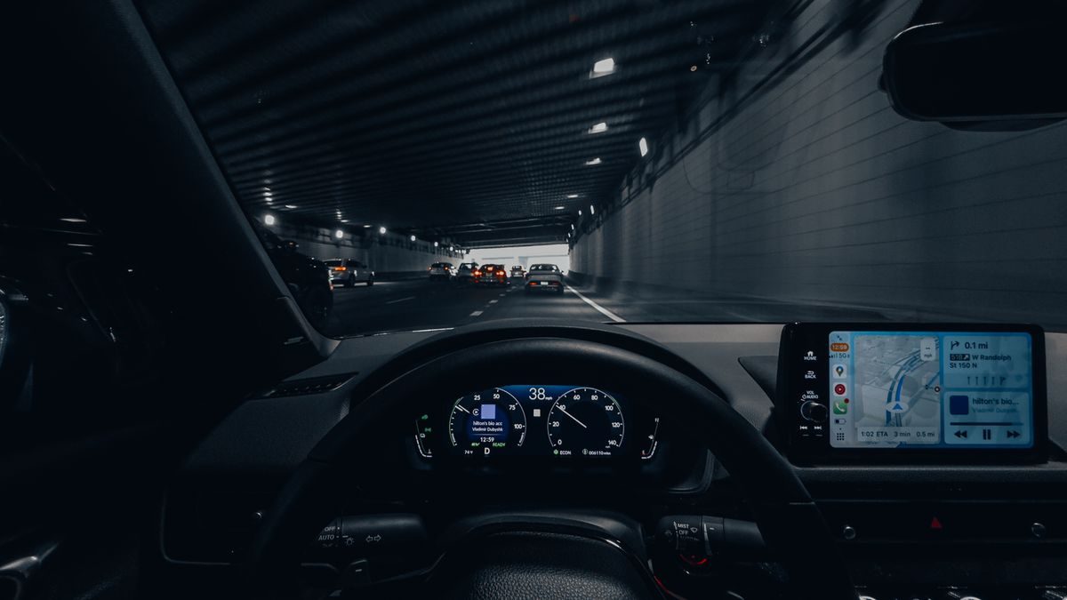 View from car dashboard driving through an illuminated city tunnel at night