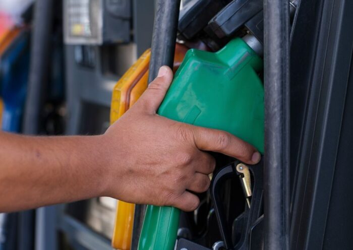 Close-up of a hand holding a green fuel nozzle at a gas pump station outdoors
