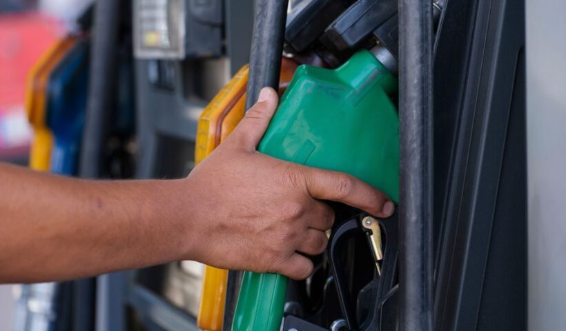 Close-up of a hand holding a green fuel nozzle at a gas pump station outdoors