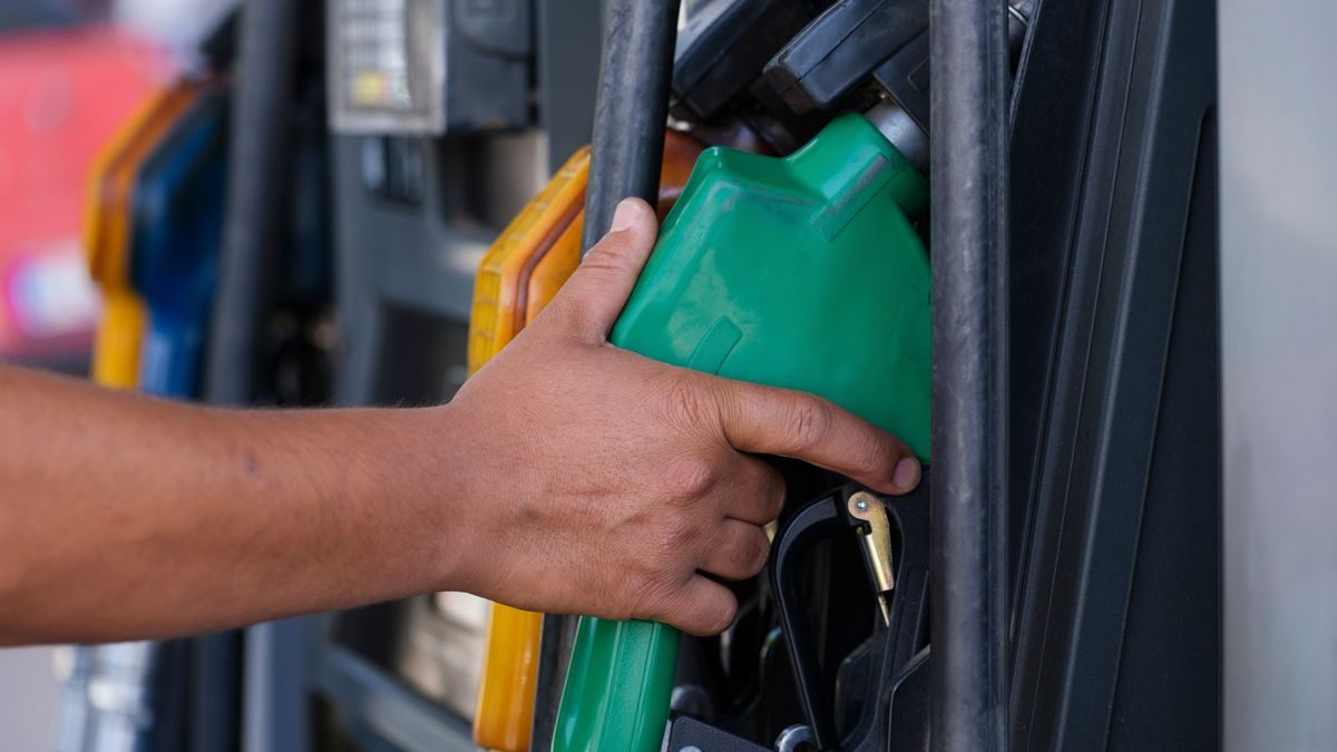 Close-up of a hand holding a green fuel nozzle at a gas pump station outdoors